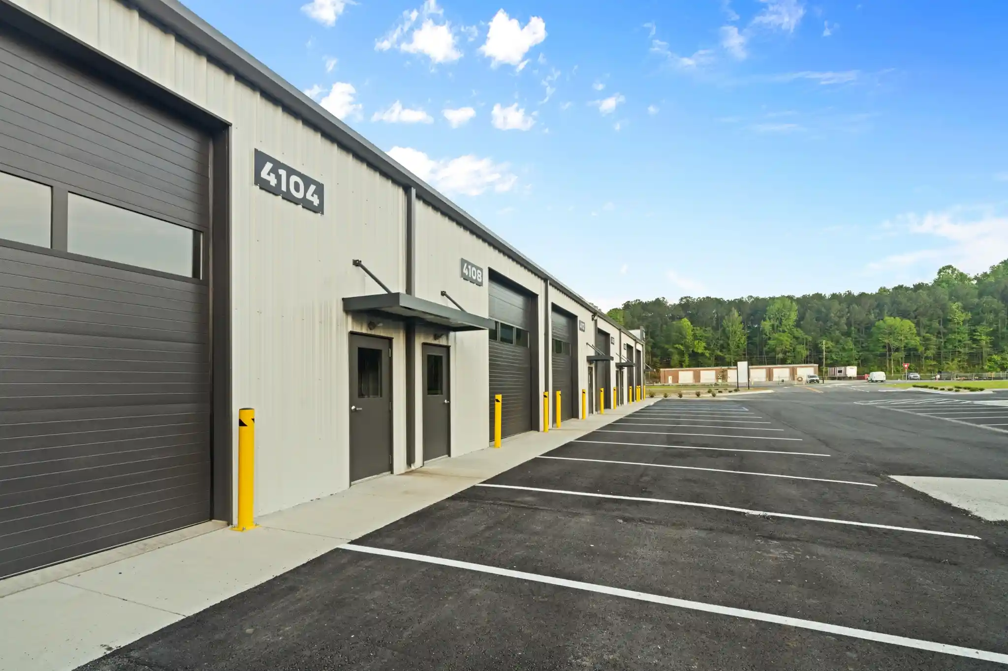Row of gray industrial storage units with doors, numbered 4104 and 4108, along a paved lot with yellow bollards.
