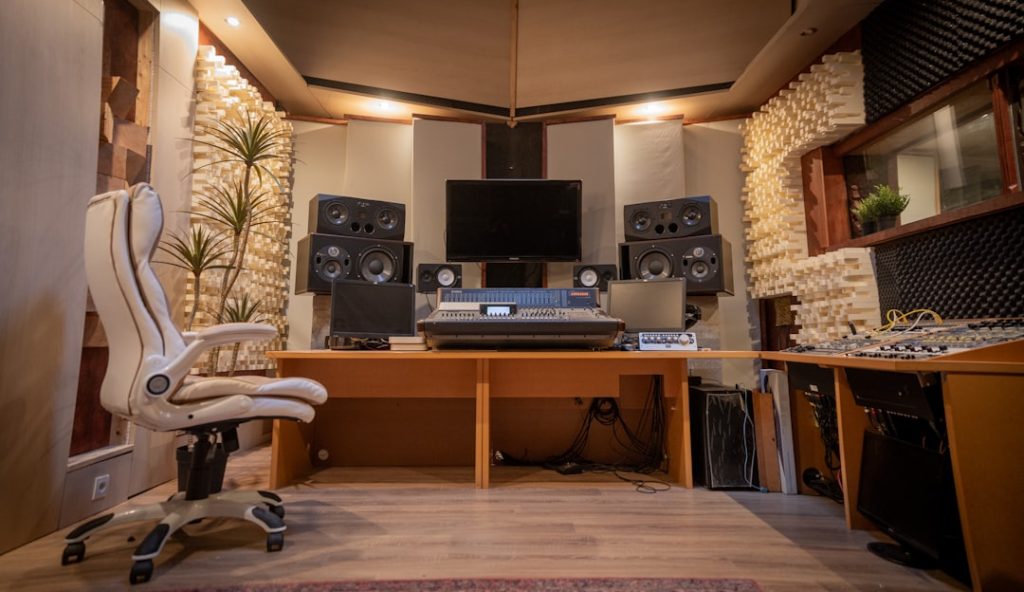 Recording studio control room with mixing console, multiple studio monitors, acoustic panels, and a white ergonomic chair.