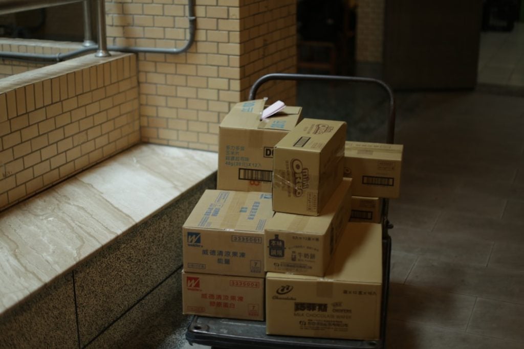 Cart loaded with stacked cardboard boxes in a brick-walled indoor hallway.