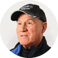 Close-up of an older man wearing a black cap with a logo and a blue jacket.
