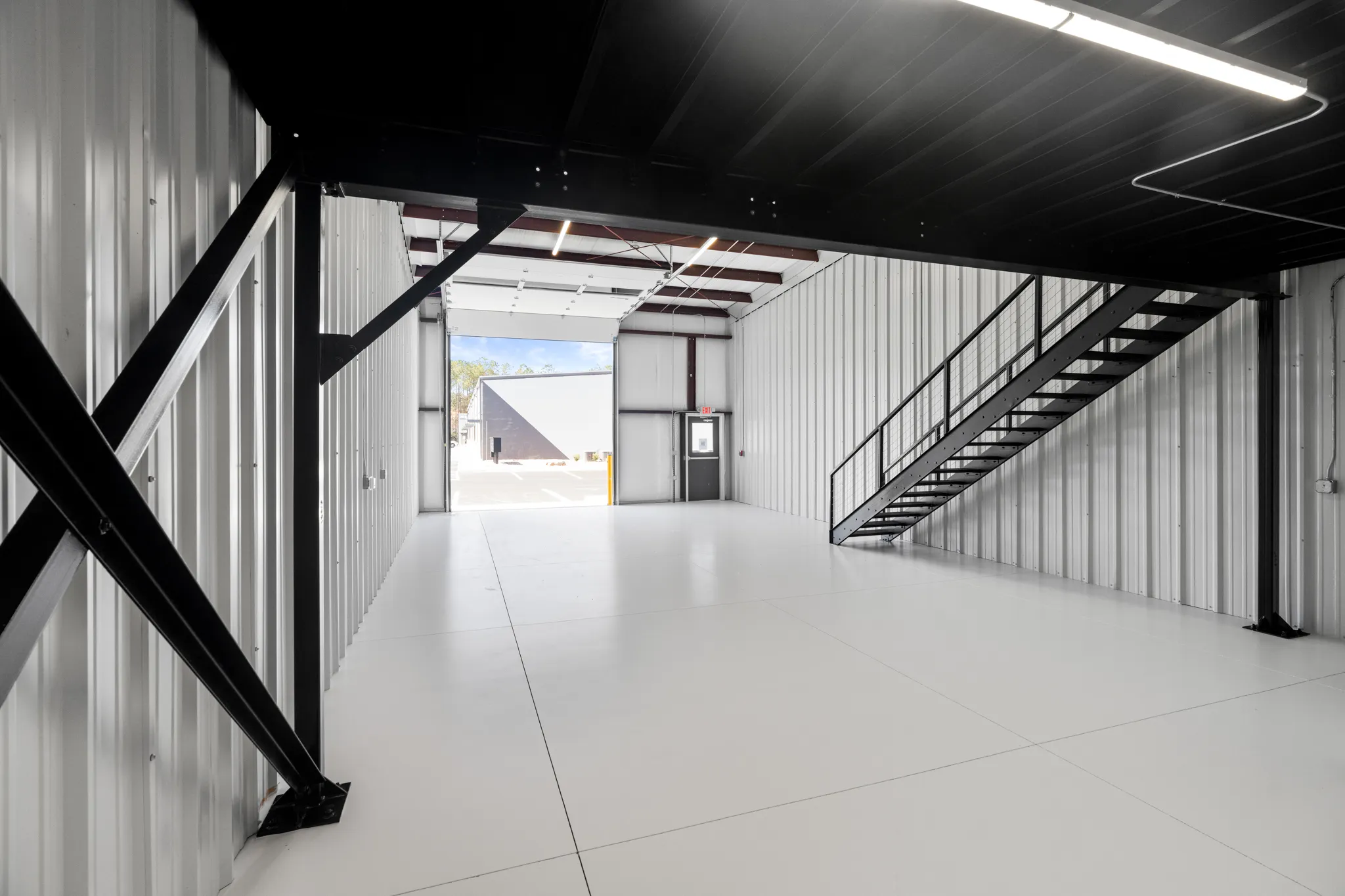 Industrial warehouse interior with black steel beams, metal walls, a diagonal brace, and a stairway to an open doorway.