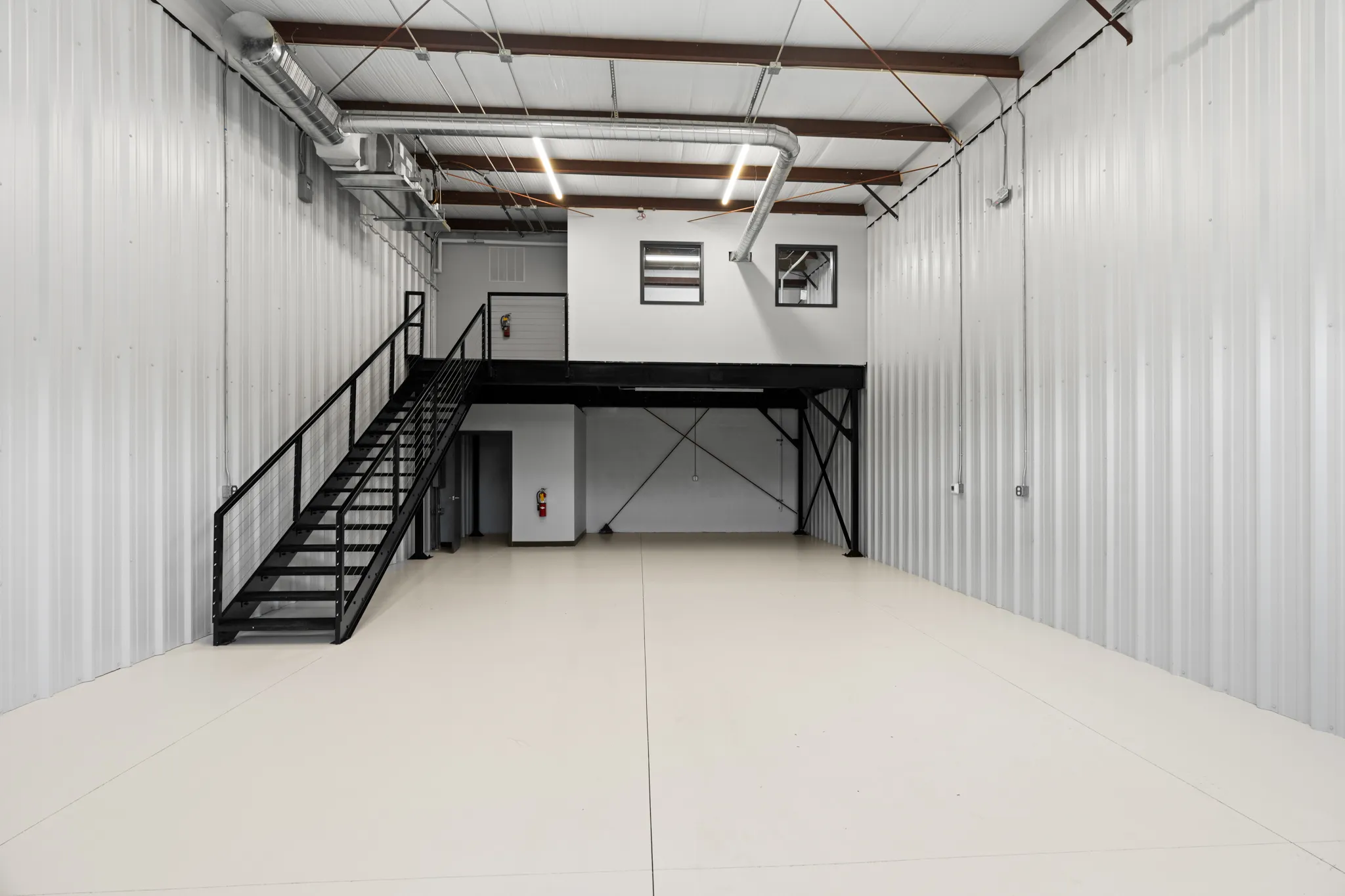Industrial warehouse interior with corrugated metal walls, mezzanine stairs, and exposed ducts.