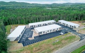 Aerial view of a modern flex warehouse campus with white-roofed units, surrounded by dense trees and a large parking lot.