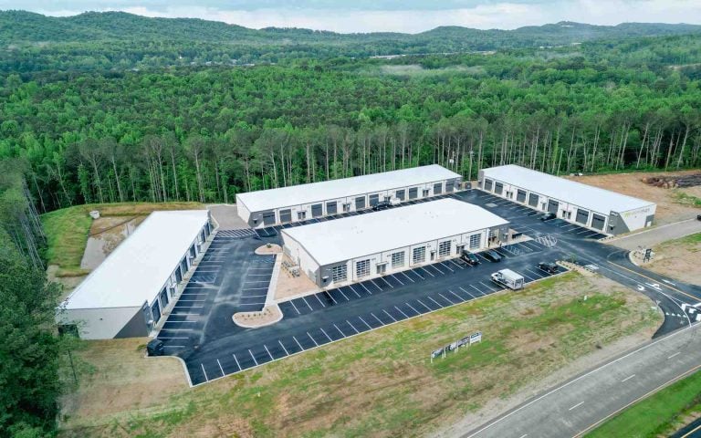 Aerial view of a modern flex warehouse campus with white-roofed units, surrounded by dense trees and a large parking lot.