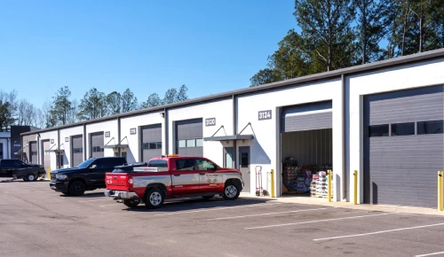 Row of storage units with gray roll-up doors; red pickup and black SUV parked in front.